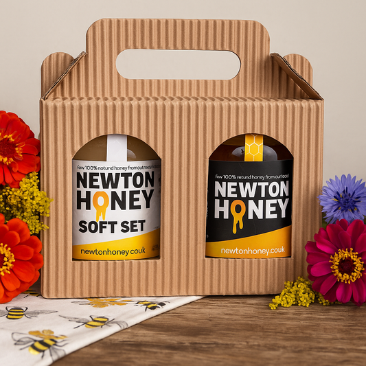 Two jars of Newton Honey in a cardboard carrier with flowers and a bee-themed mat.