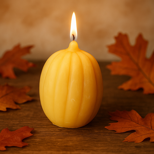 Lit pumpkin-shaped beeswax candle on rustic wooden table with autumn leaves – handmade, eco-friendly, natural honey aroma