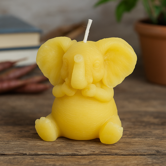 Styled photograph of a handcrafted yellow elephant-shaped beeswax candle from Newton Honey, displayed on a rustic wooden surface with honey jars and dried flowers in soft natural light.