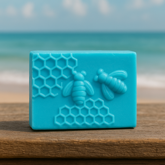 Ocean Fresh beeswax and honey soap bar with embossed bees and honeycomb design, displayed on rustic wooden table by the seaside.